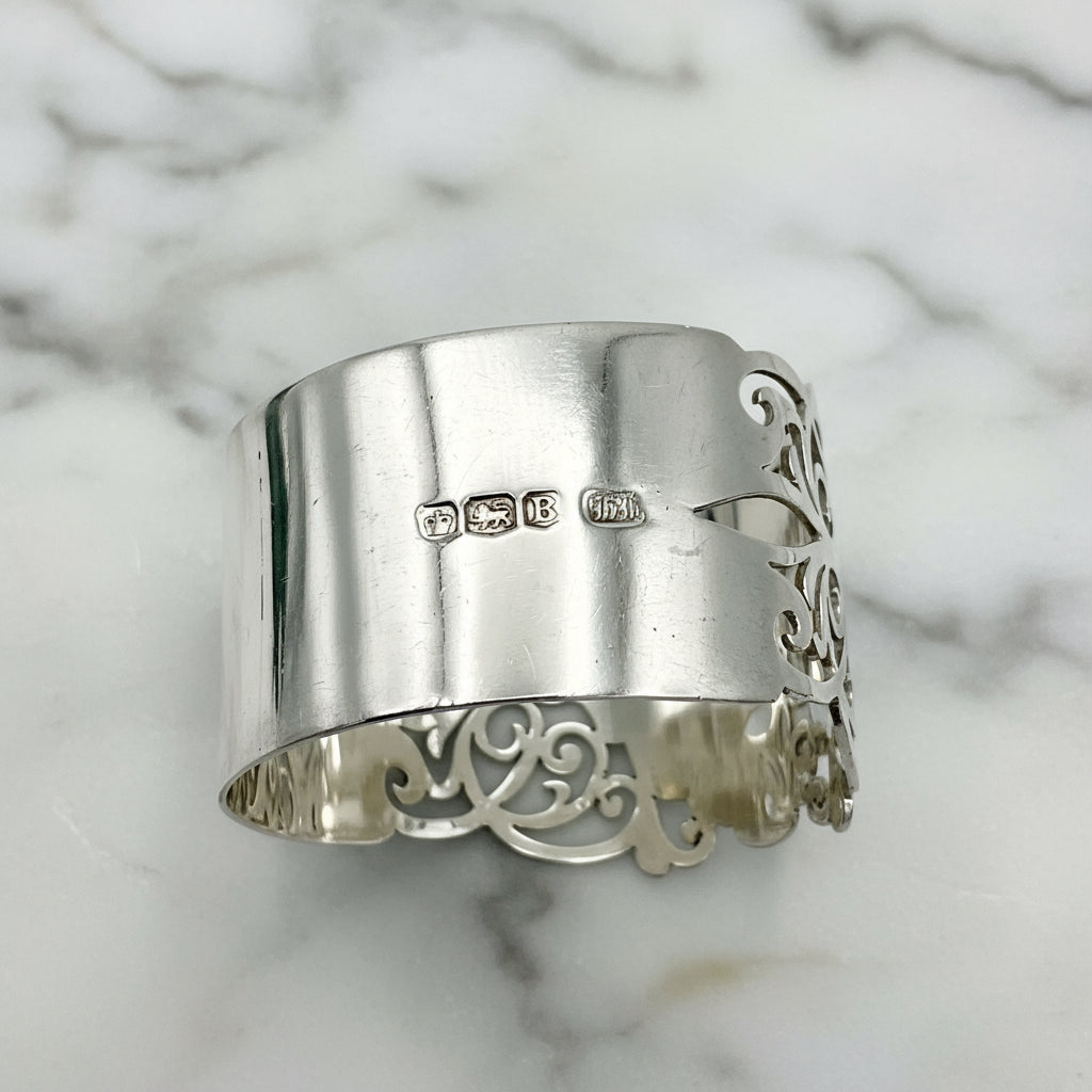 Shiny napkin ring with elaborate sides and hallmarks on a plain background 
