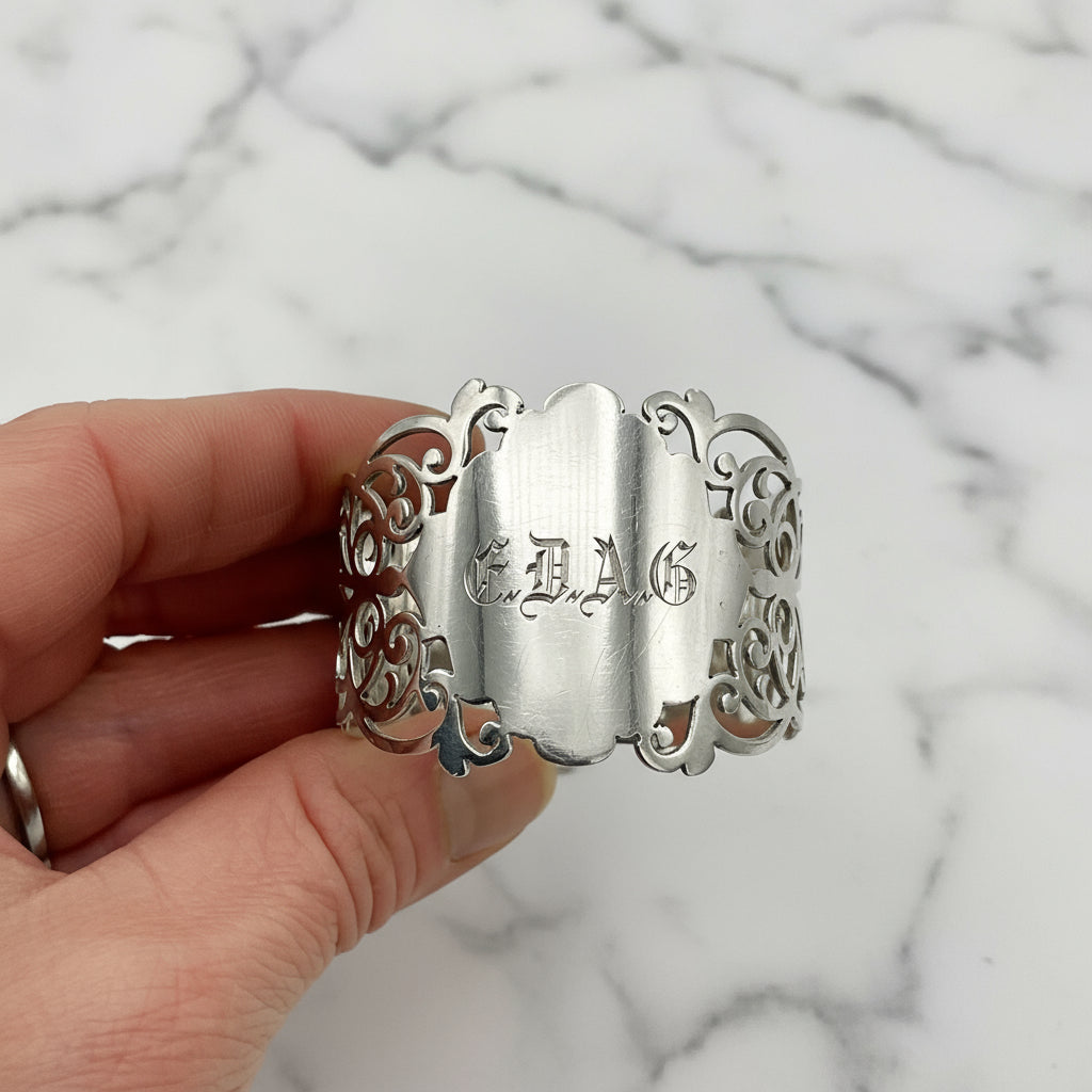 Shiny napkin ring with elaborate sides and EDAG in the centre held in a hand on a plain background 