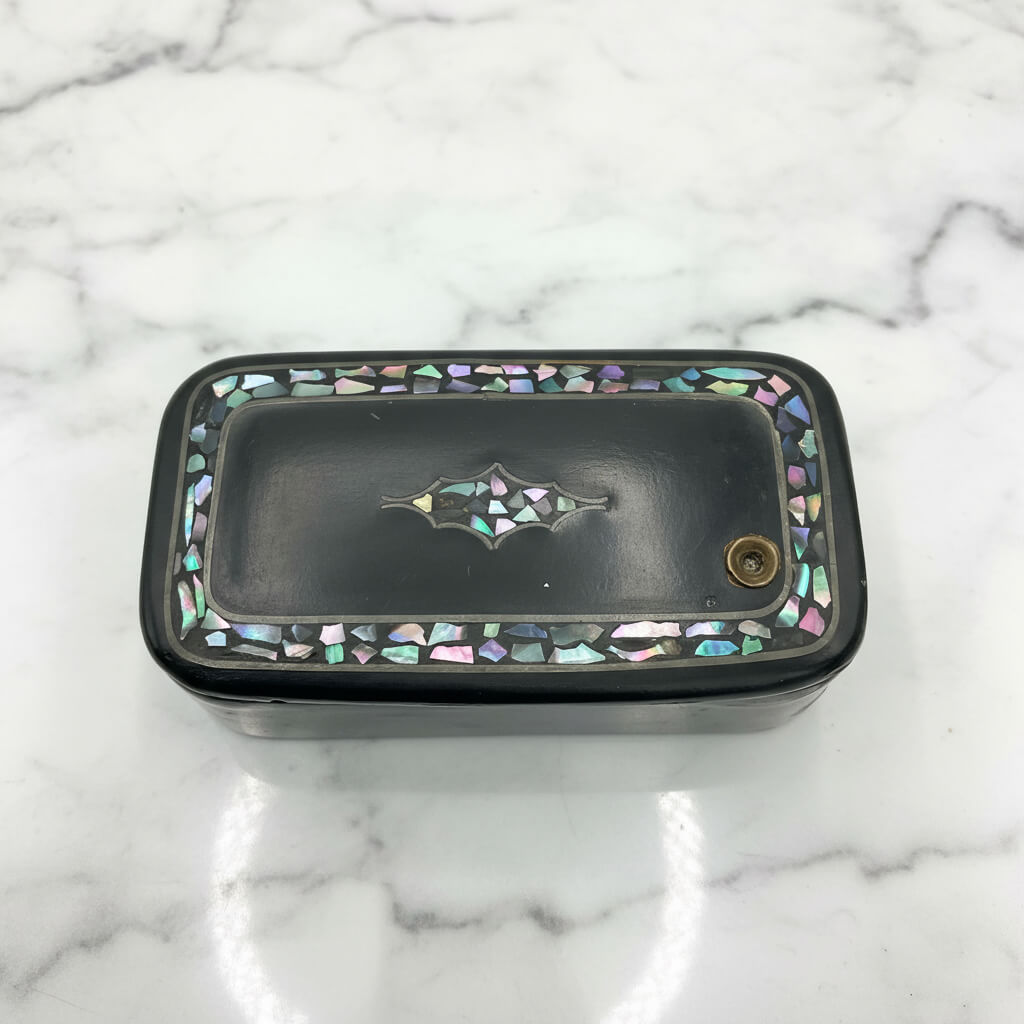 Antique black lacquer snuff box with multicoloured shell inlay on a plain background 