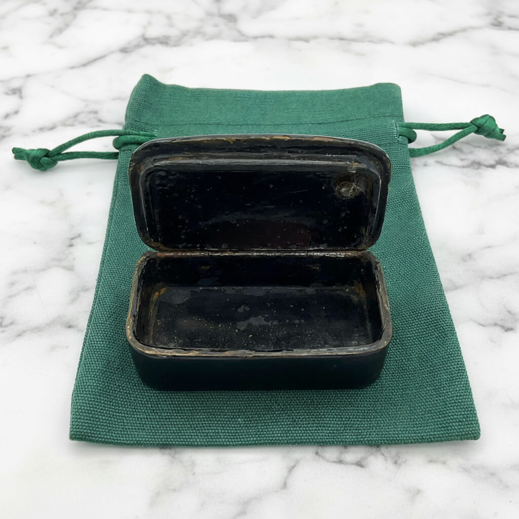 Lid open of Antique black lacquer snuff box showing interior on a green gift bag