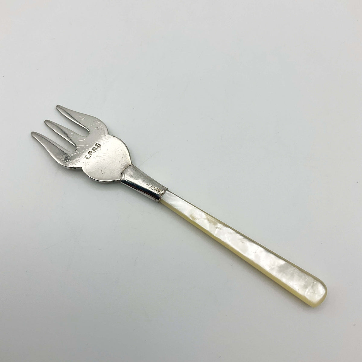 Small silver-plated olive pickle fork with a mother of pearl handle by Beeches Vintage, showing detailed craftsmanship.
