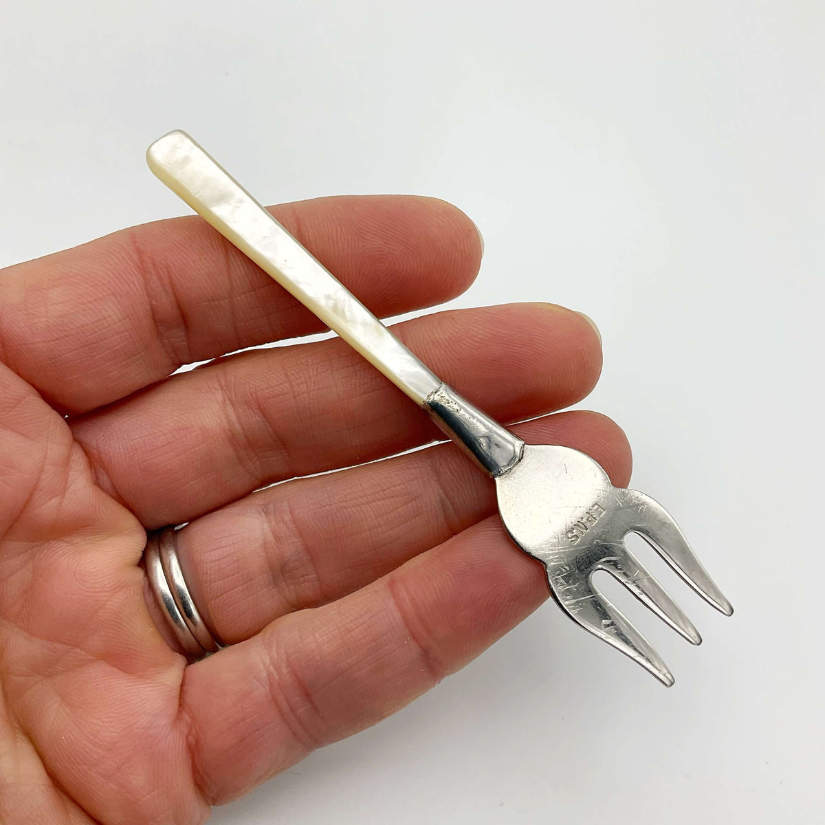 Small silver-plated olive pickle fork with a mother of pearl handle, designed for serving olives and small appetizers.