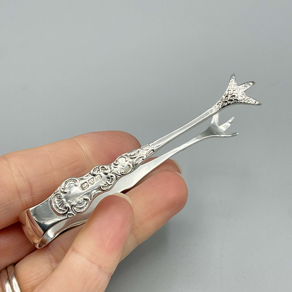 Antique 1902 small sterling silver sugar tongs with ornate design, crafted by Beeches Vintage, featuring intricate detailing.