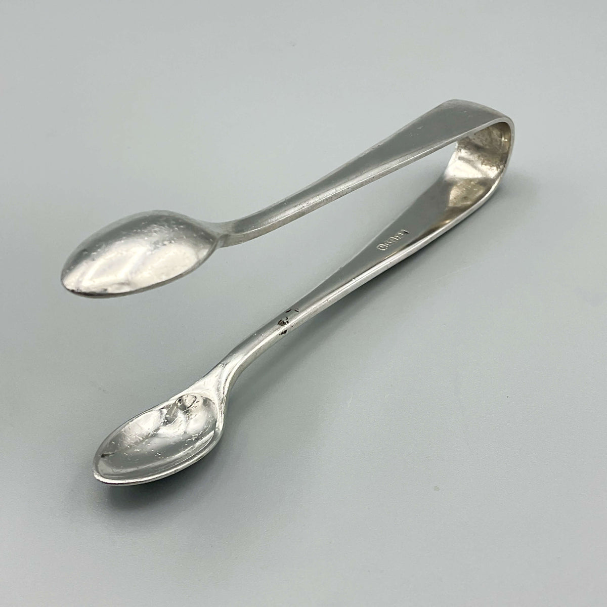 Vintage Silver Plated Sugar Tongs from Beeches Vintage, showing elegant design and shiny finish on a reflective surface.