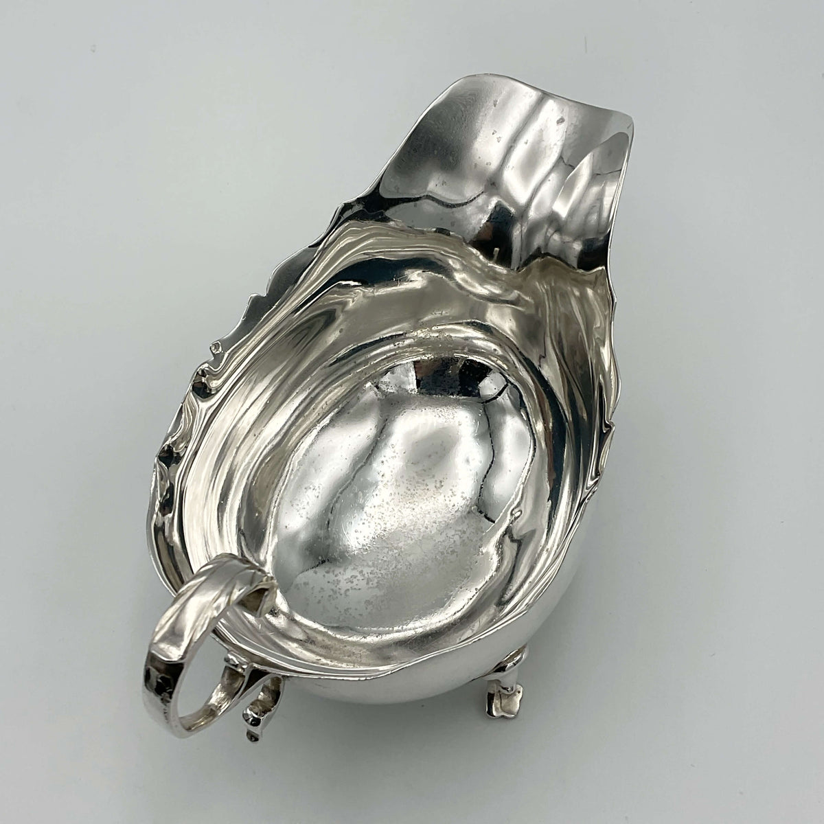 Antique 1902 solid silver sauce boat with ornate design, crafted by Beeches Vintage, displayed on a polished surface.