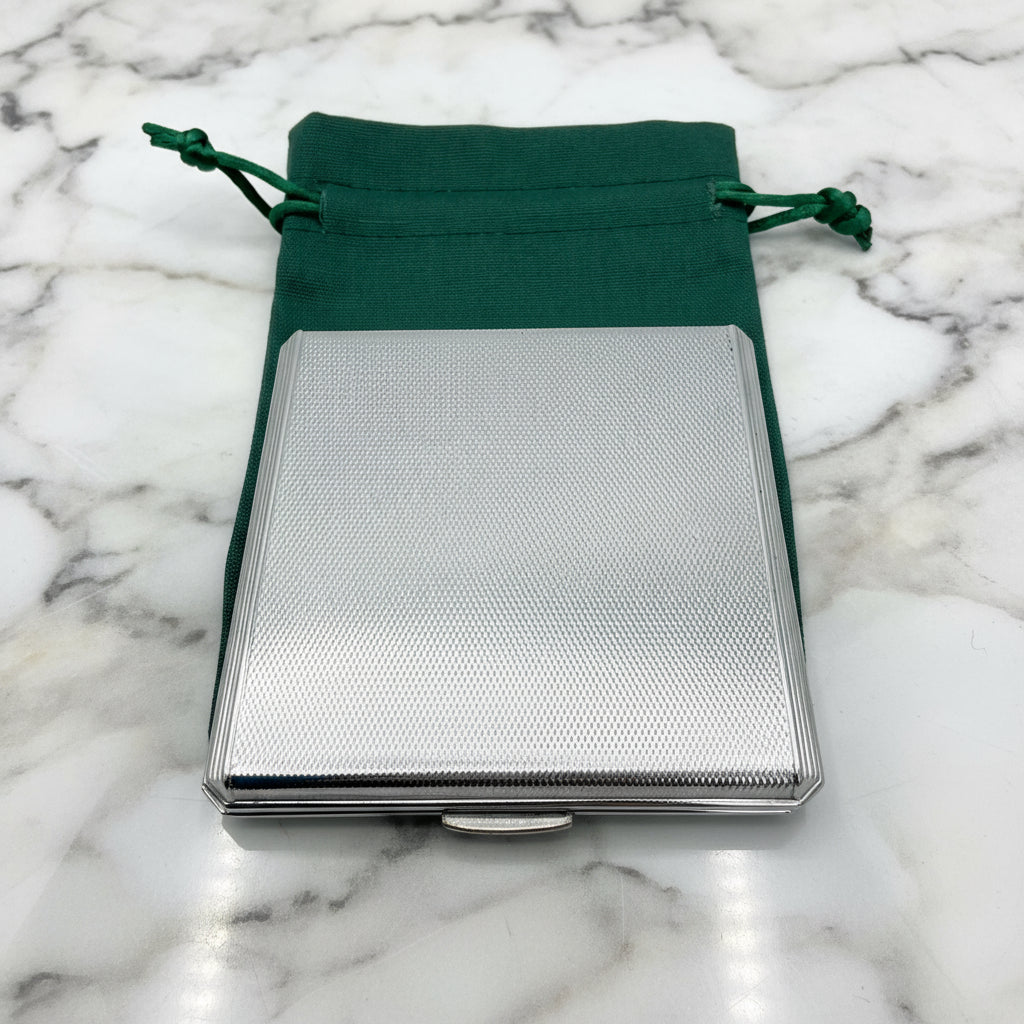 silver compact on a green bag on a marble background