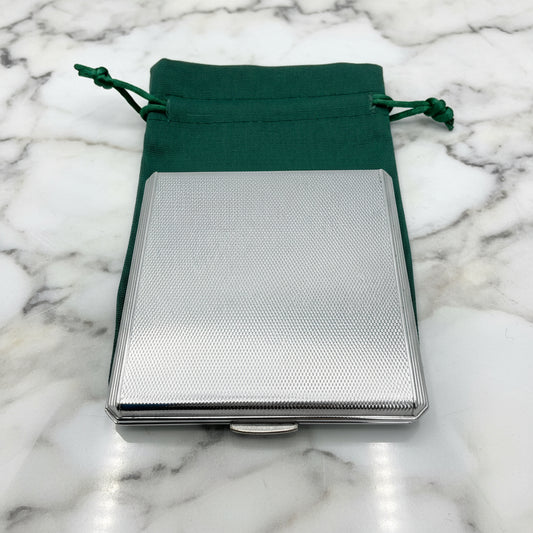 silver compact on a green bag on a marble background
