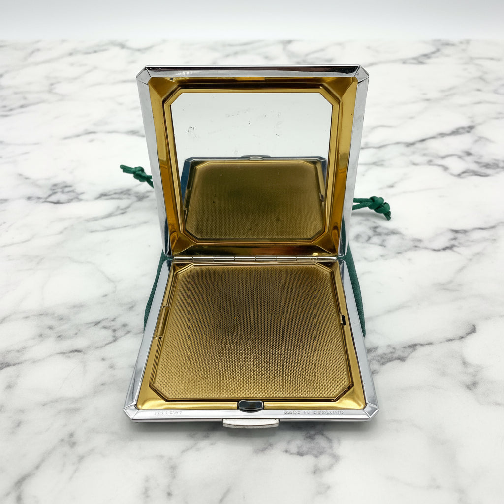 Open powder compact showing mirror and gold interior on green bag and marble background