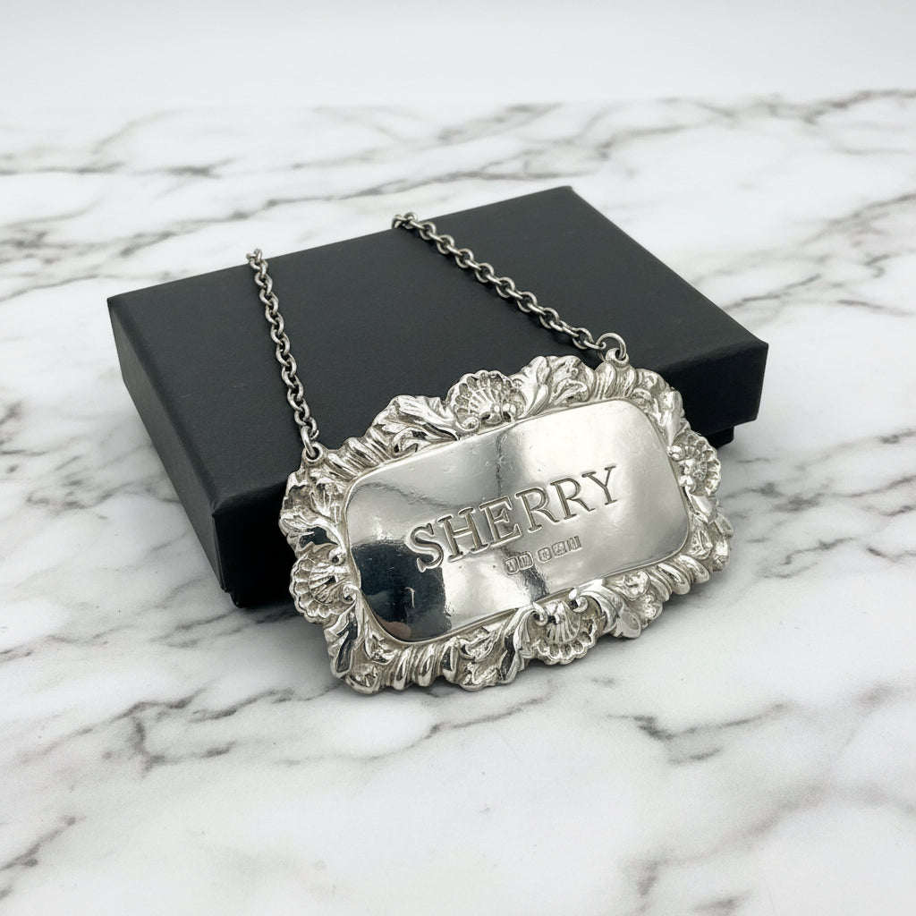 A shiny Sherry decanter label in front of a black presentation box on a marble background.