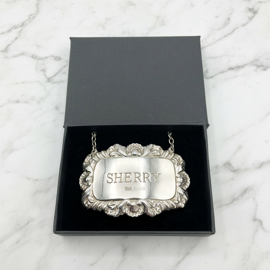 A shiny Sherry decanter label in a black presentation box on a marble background.