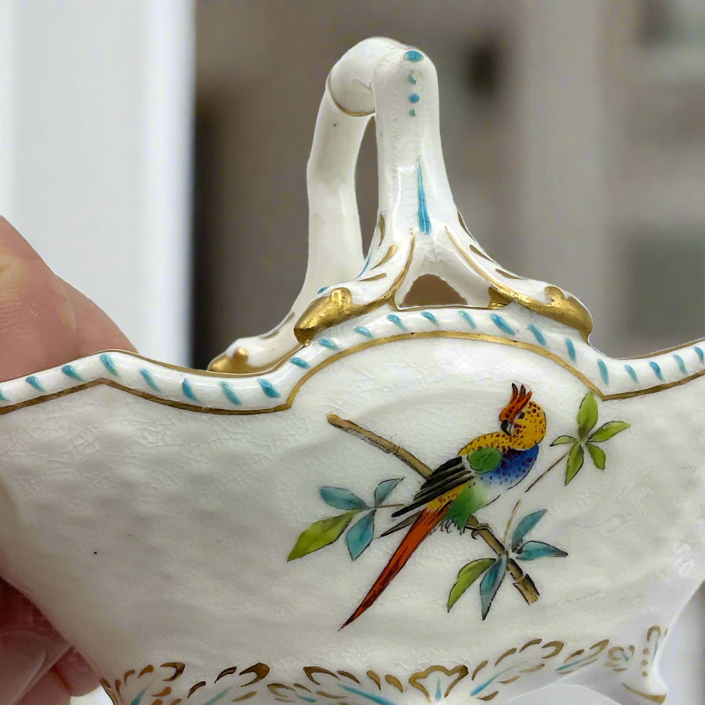 side view of china basket ornament with parrot on the side held in a hand with a room in the background