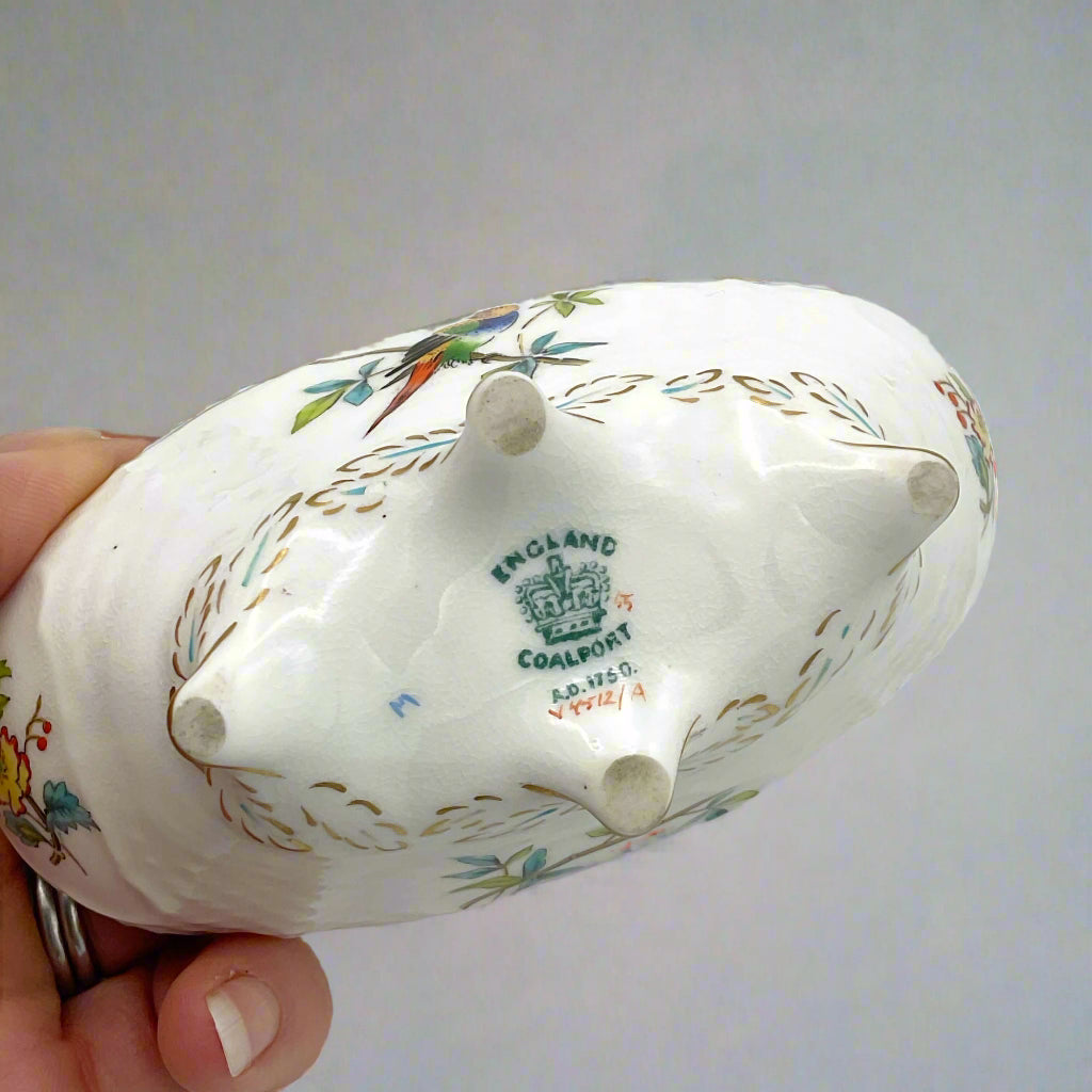 base of ornament with England and Coalport imprinted and held in a hand  with a grey background