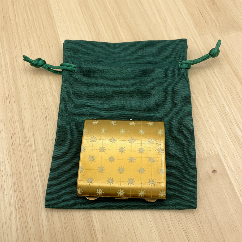 gold powder compact on green bag on a wood table