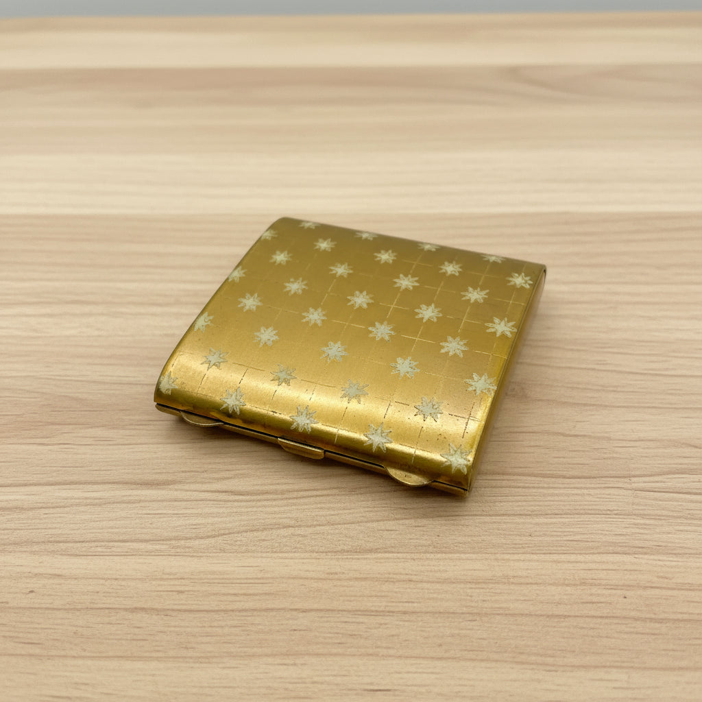 A vintage Zenette mini mirror compact from the 1940s with a gold-colored brass exterior, cream Art Deco stars design, and an etched stars pattern on the base. It is open, showing the mirror and the brand name 'Zenette' inscribed above it.