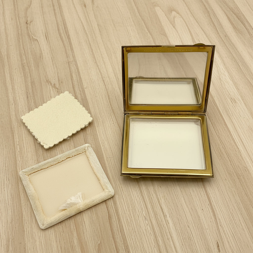 open powder compact with powder screen and powder puff on a wood table