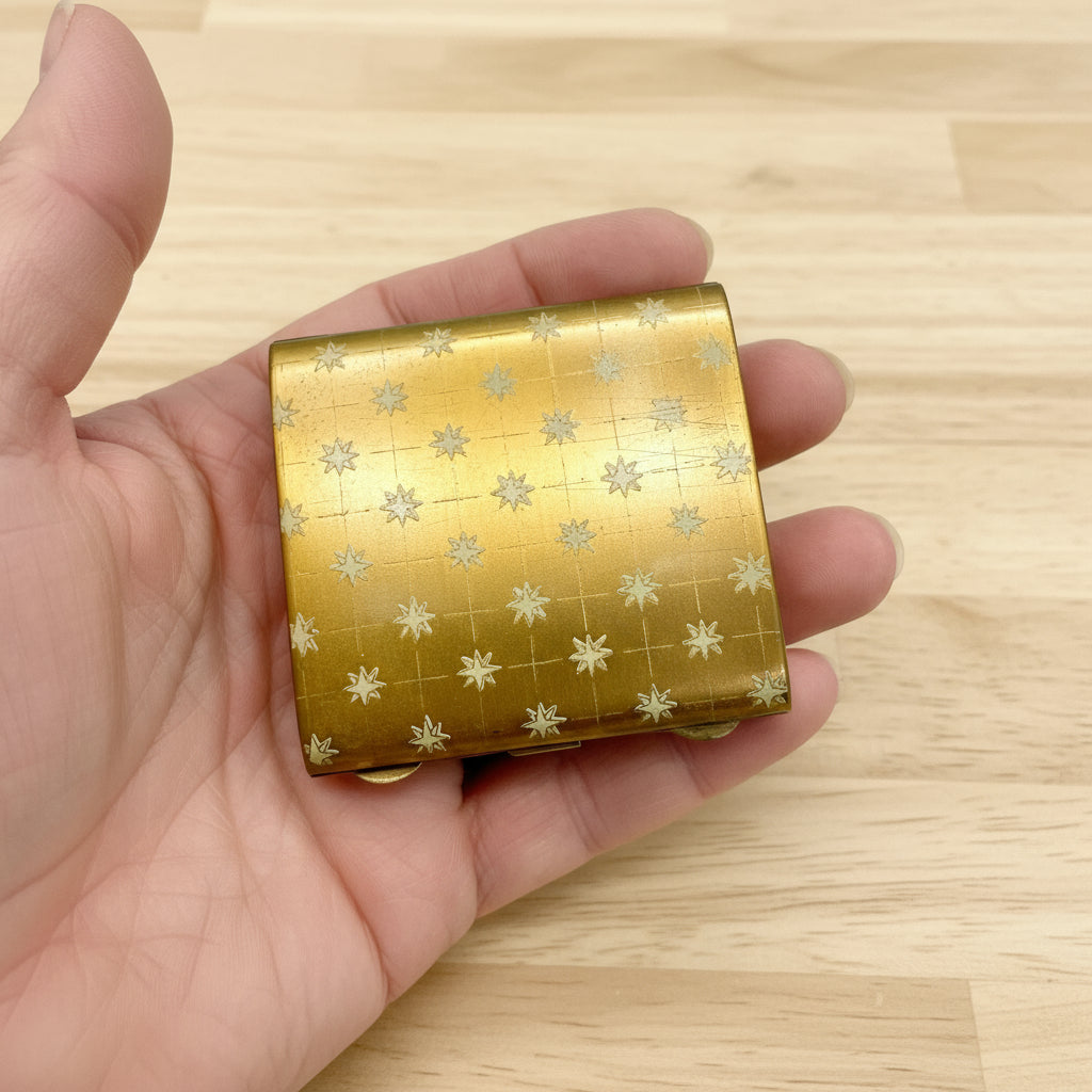 gold powder compact held in han with wood table in background