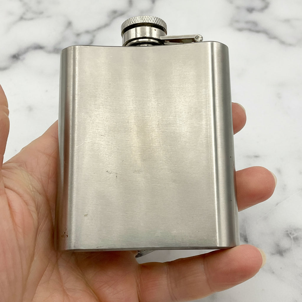 Back of steel hip flask held in a hand with a marble background