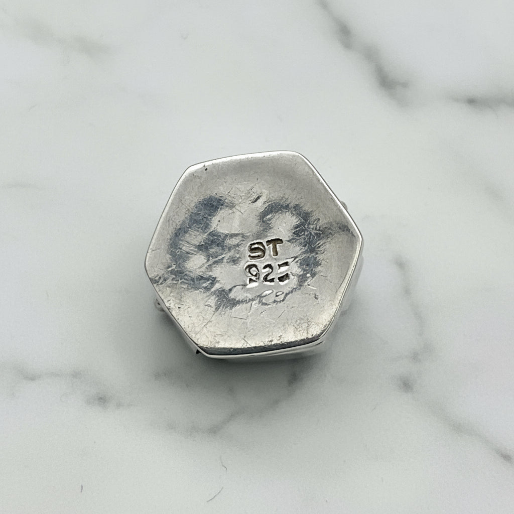 Base of silver hexagonal pill box with ST 925 imprinted on a marble surface