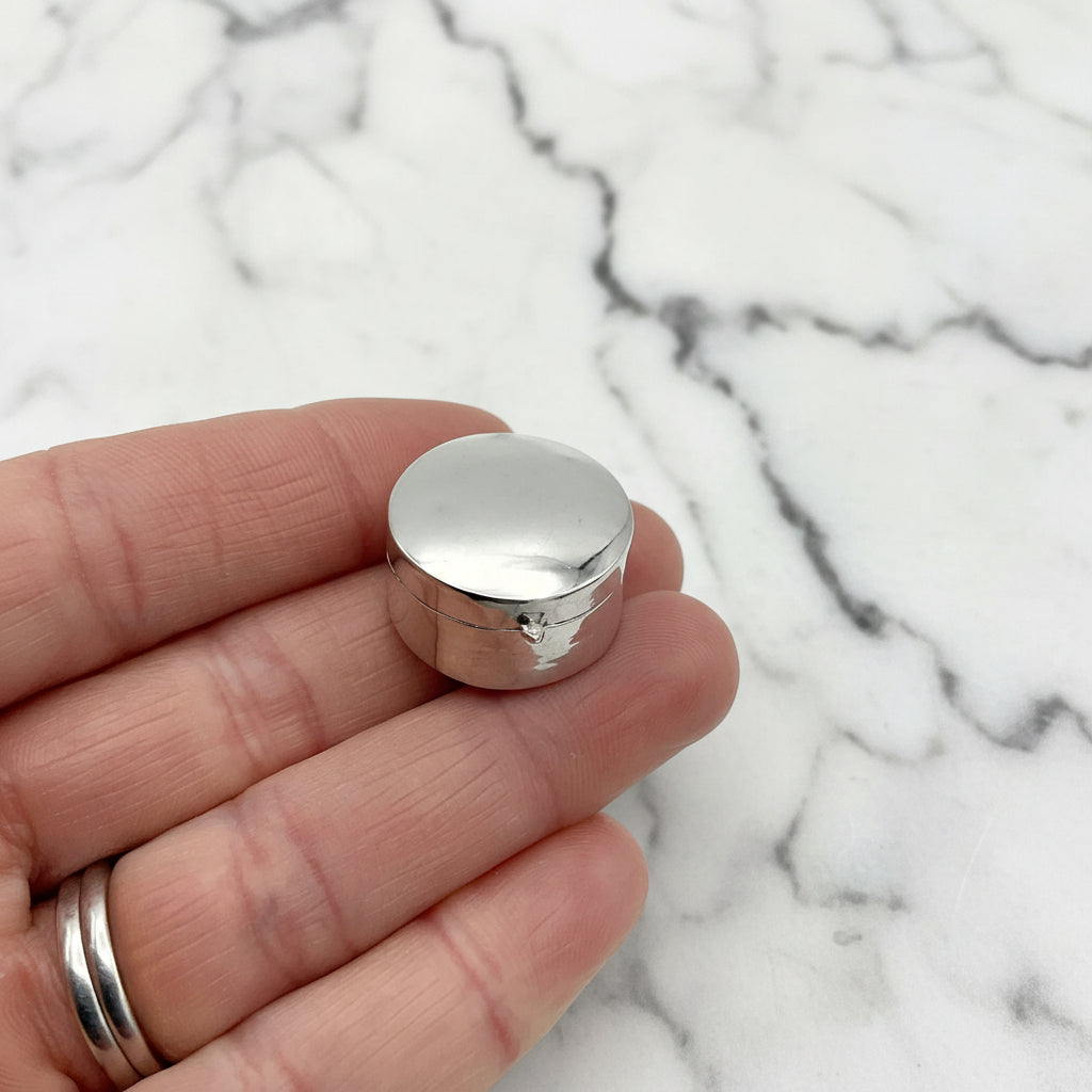 small silver pill box on fingertips with marble background