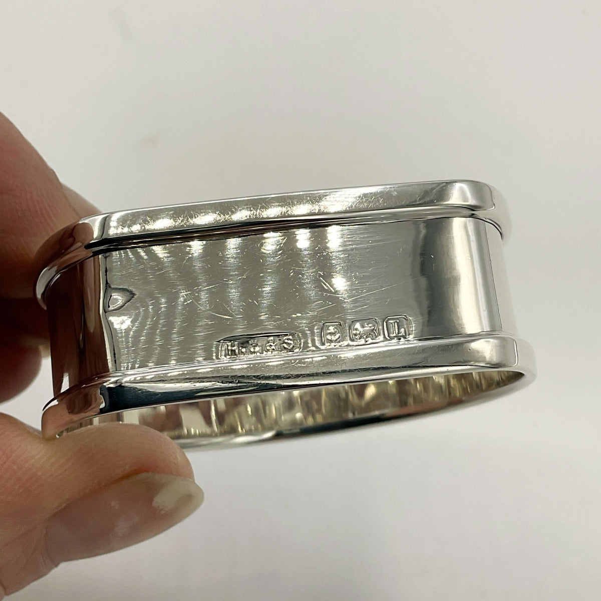 Back view of Vintage silver napkin ring held in fingers on a white background