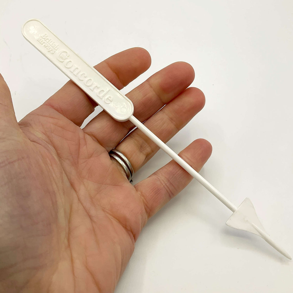 White Concorde Swizzle stick in a hand with a white background 