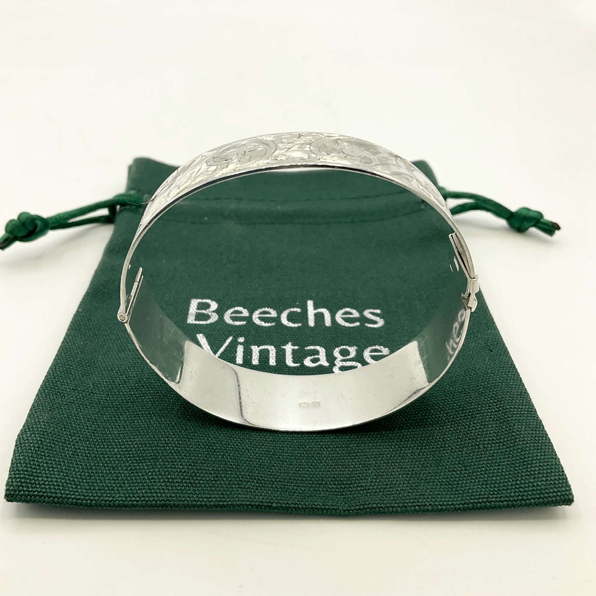 Side view of a Silver Art Nouveau design bracelet on a green gift bag on a white background.