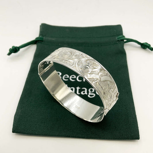Silver Art Nouveau design bracelet on a green gift bag on a white background.