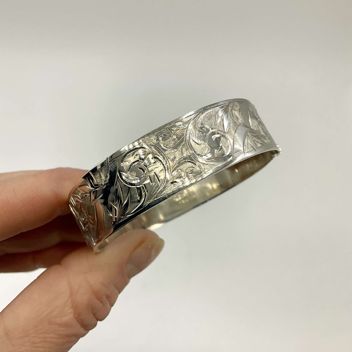 Silver Art Nouveau design bracelet held in fingers on a white background.