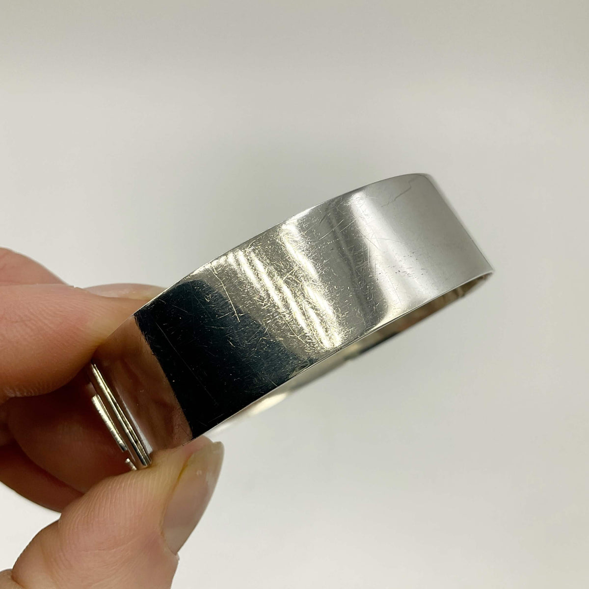 Silver bangle bracelet held in fingers on a white background.