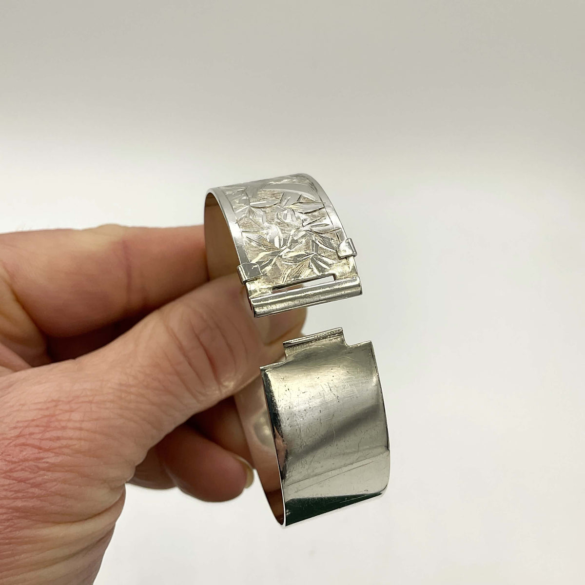 Open clasp of the Silver Art Nouveau design bracelet held in fingers on a white background.