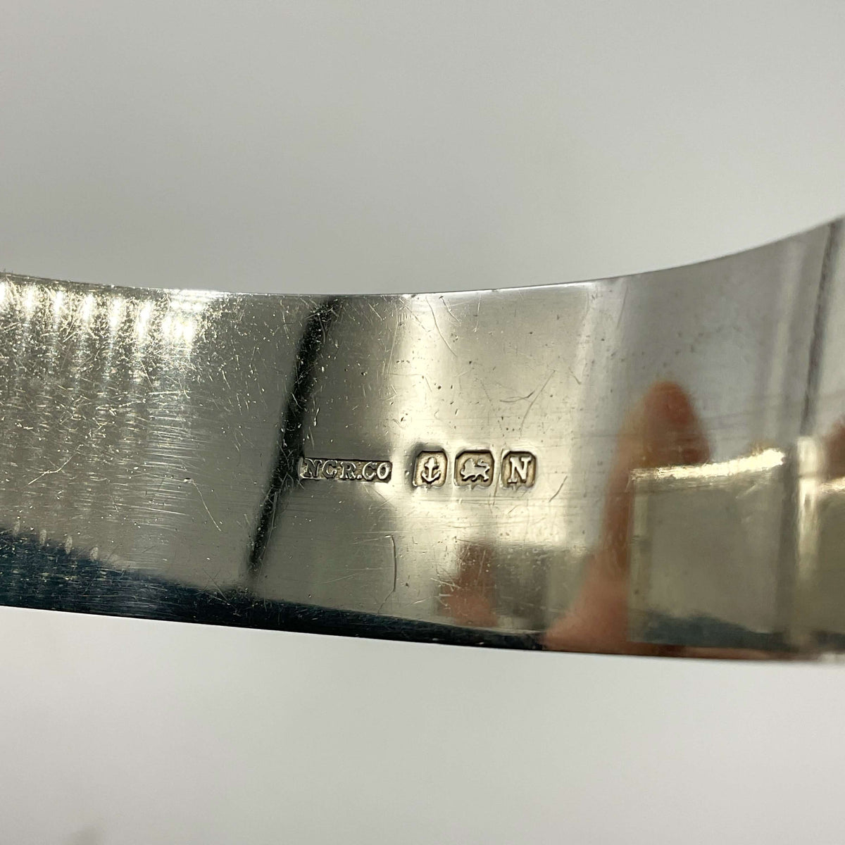 Inside of Silver bracelet showing the makerr’s mark and hallmarks on a white background.