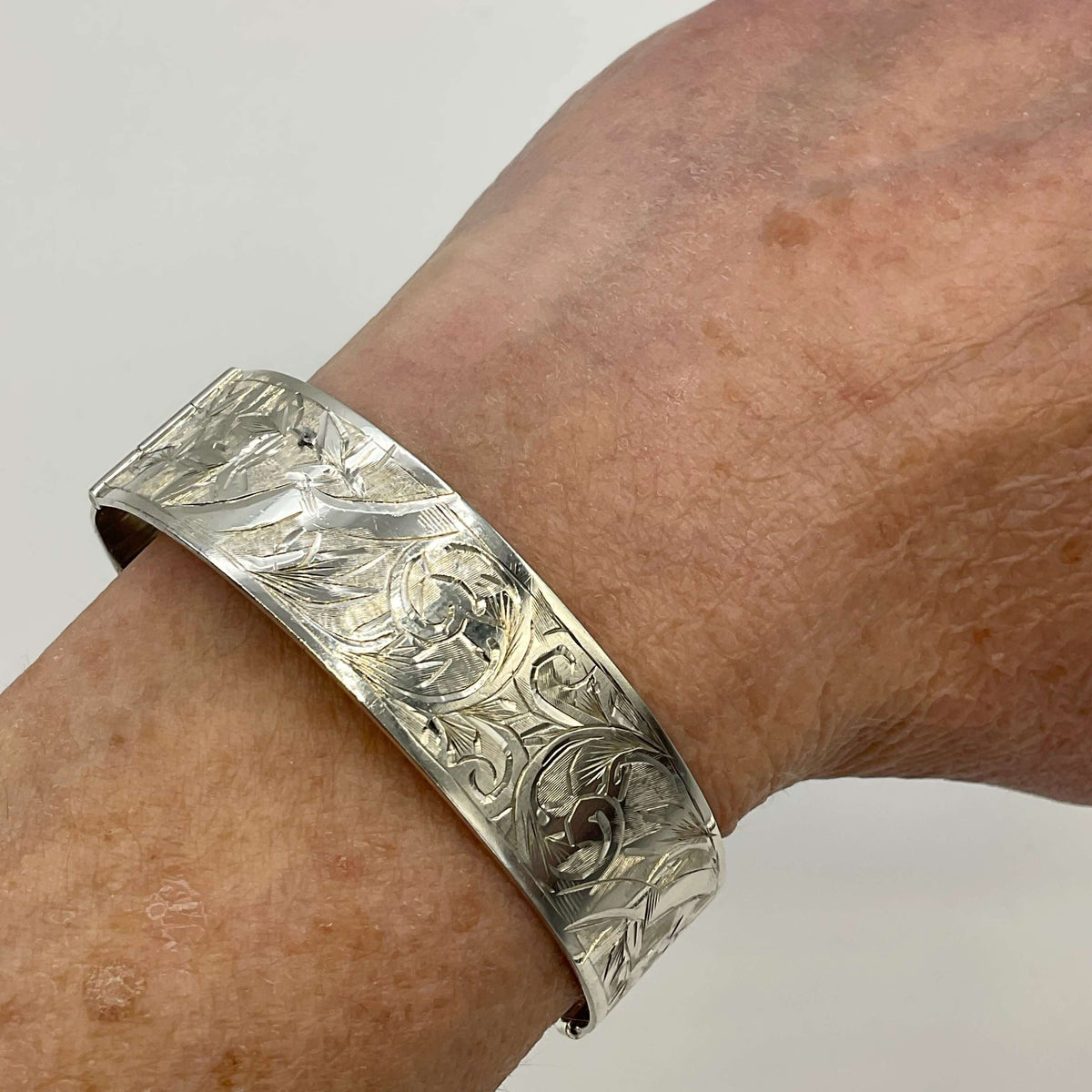 Silver Art Nouveau design bracelet on a wrist on a white background.
