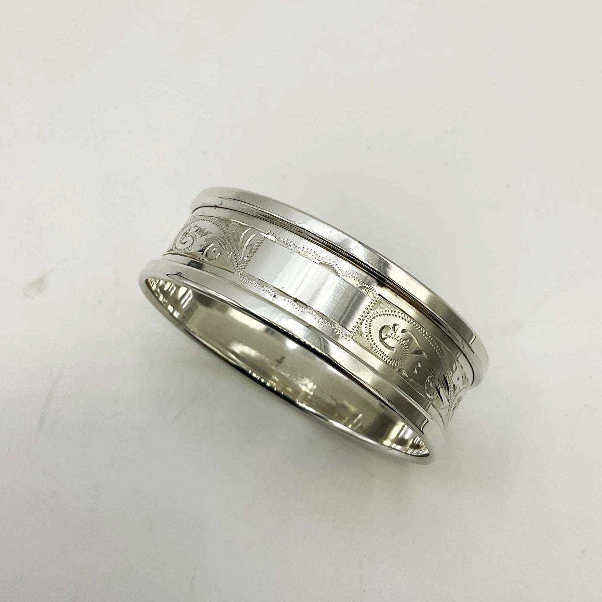 Silver napkin ring with a leaf scroll design on a white background 