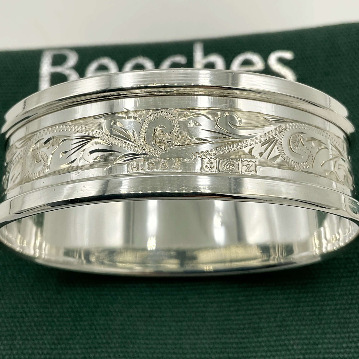 Silver napkin ring with a leaf scroll design on a green gift bag and white background 