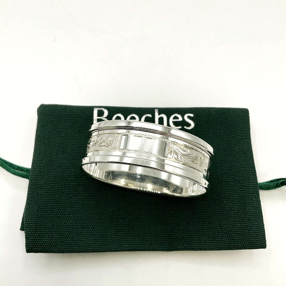 Silver napkin ring with a leaf scroll design on a green gift bag and white background 