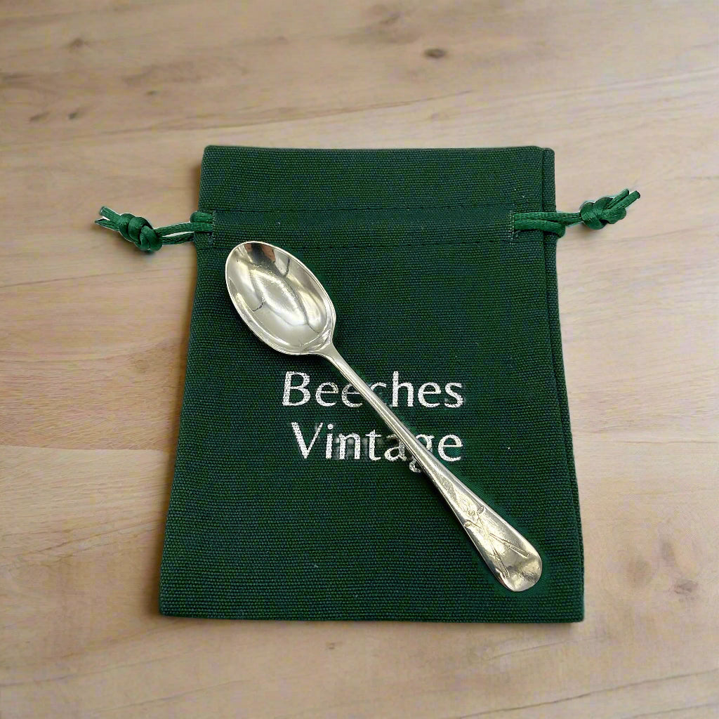 Silver coffee spoon on a green gift bag on a wood background 