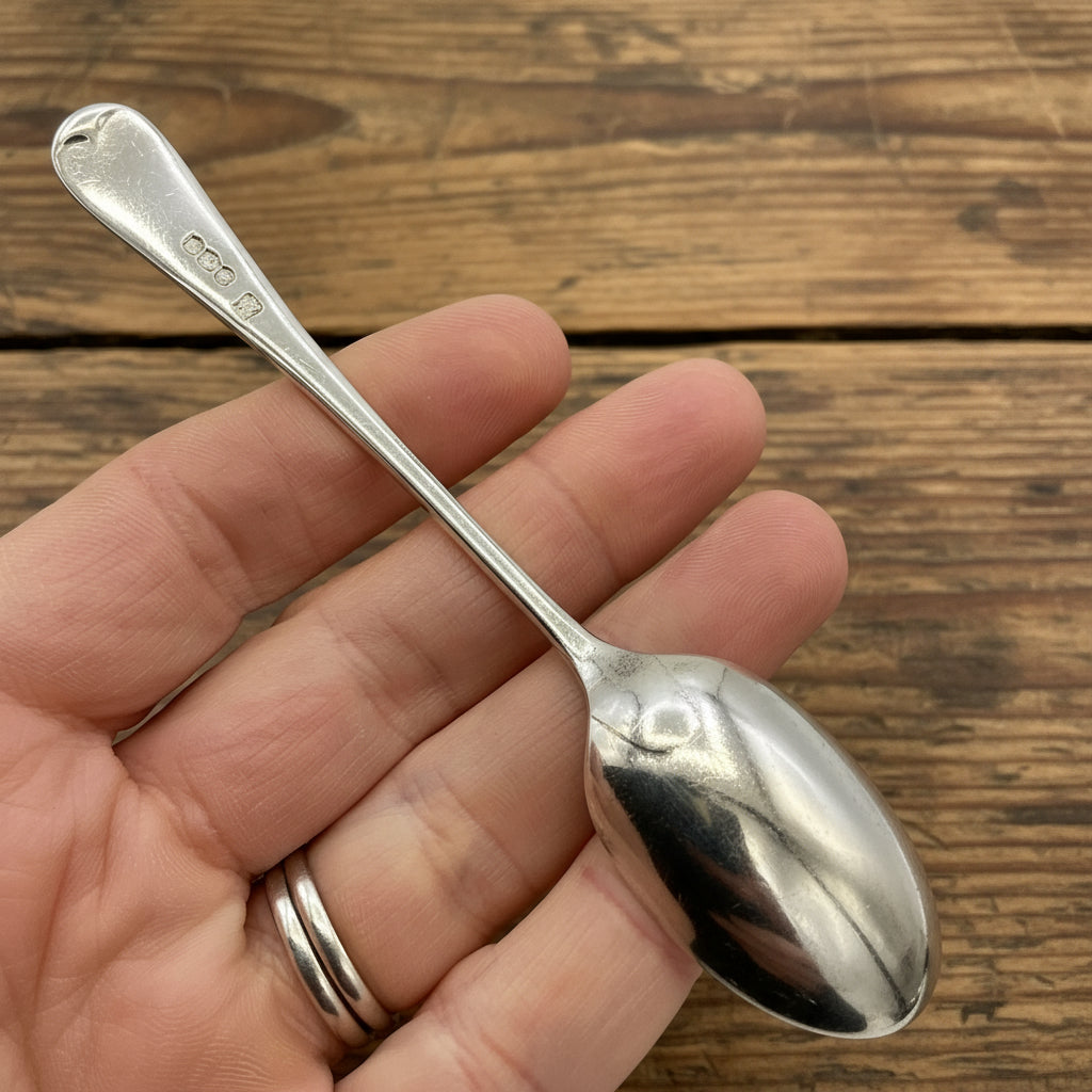 Back of an antique silver spoon held in a hand on a white background 