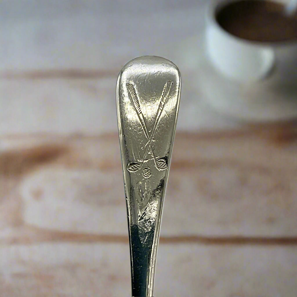 Handle of Silver coffee spoon showing a golf club motif on a wood table background 