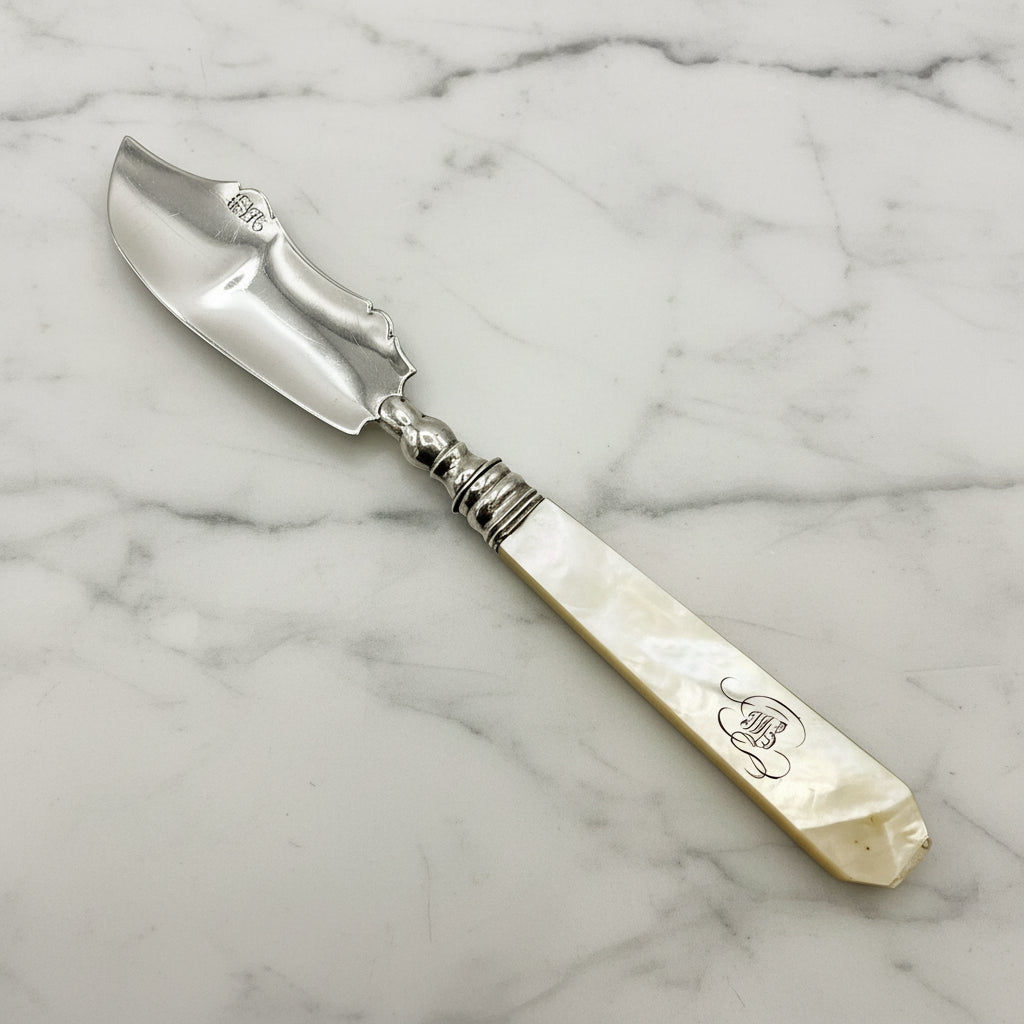 Antique silver and mother of pearl butter knife on a marble worktop