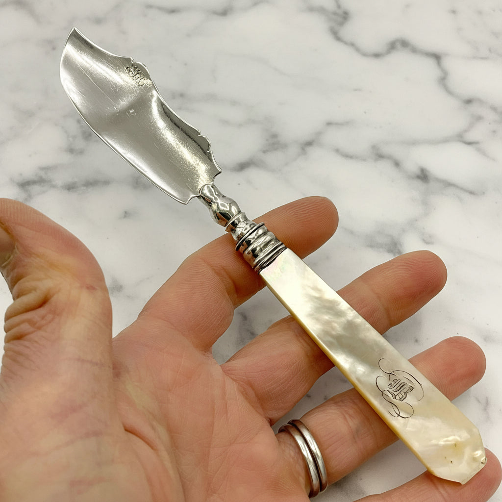 Antique silver and mother of pearl butter knife held in a hand on a marble  background 