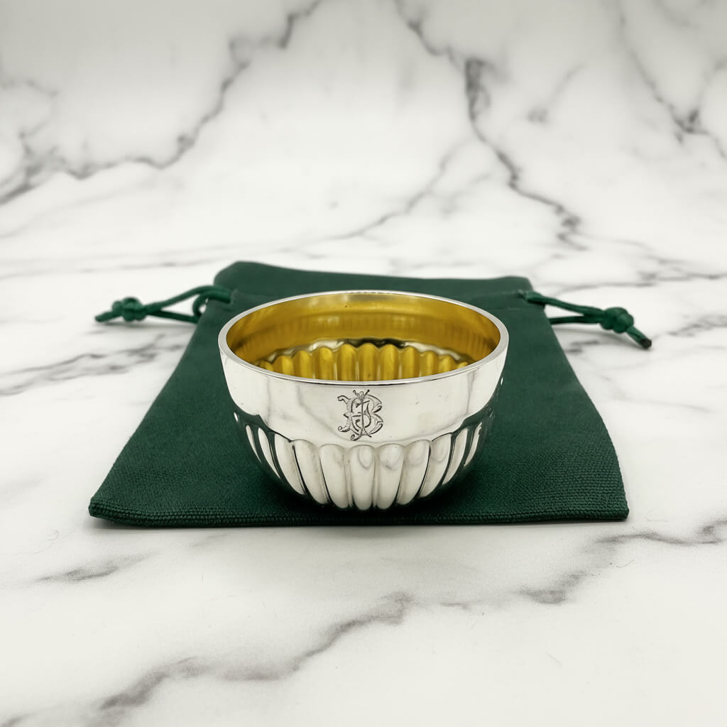 Silver bowl with gold interior on a green fabric pouch on a marble background