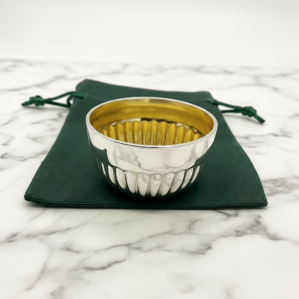 Silver textured bowl with gold interior on green fabric pouch on a marble surface