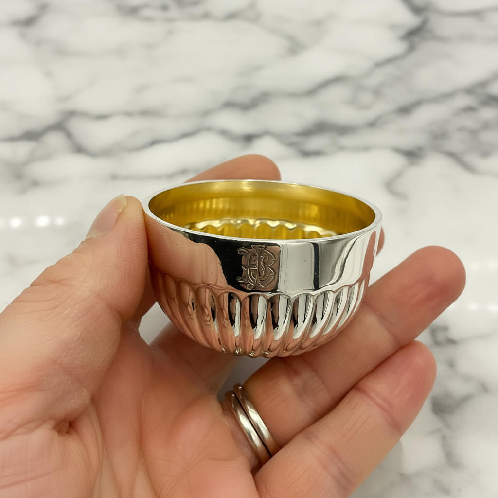 Silver textured bowl with gold interior held in hand against a marble background.