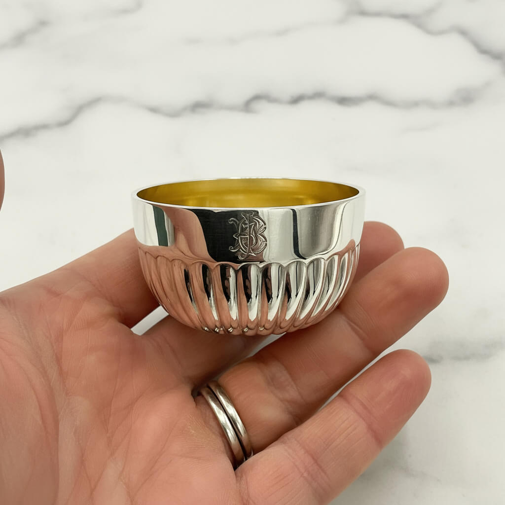 Silver bowl with a engraved design held in a hand on a marble background