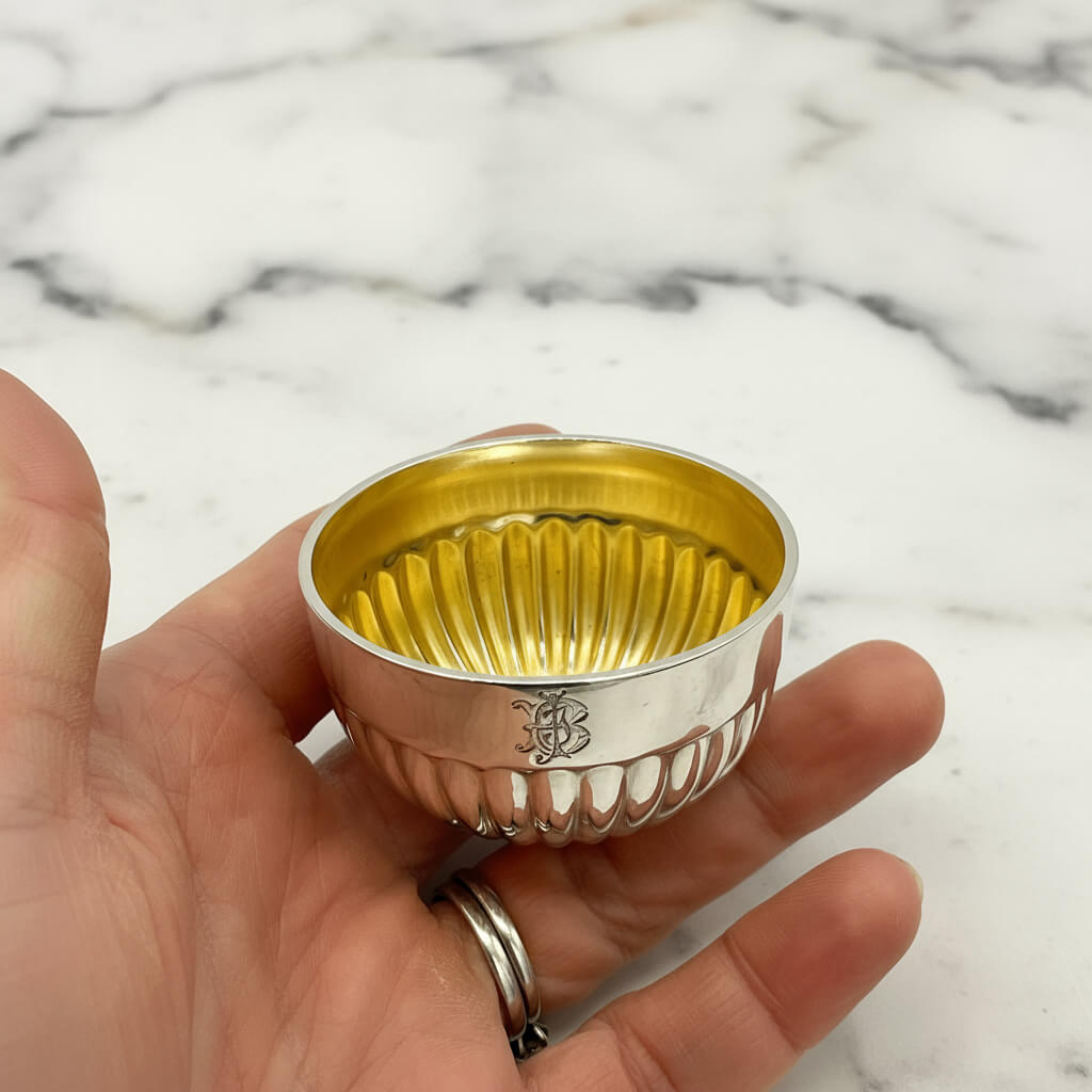 Small silver bowl with gold interior held in a hand on a marble background
