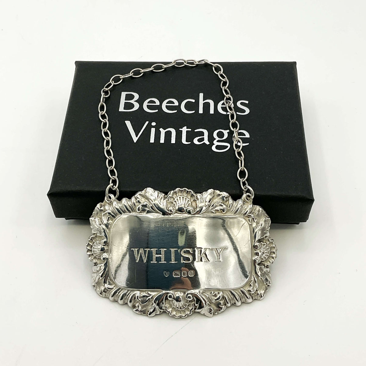 Silver whisky decanter label Leaning on a black presentation box and a white background 
