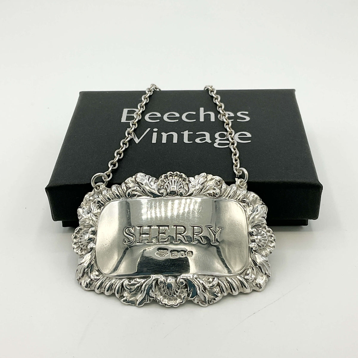 Silver Sherry decanter label in front of a black presentation box with a white background 