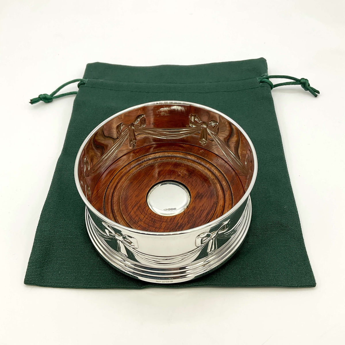 Silver and wooden bottle coaster on a green drawstring bag and marble worktop