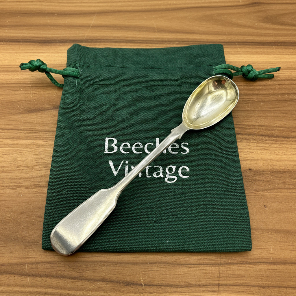 Antique silver salt spoon on a green gift bag with a wood background 