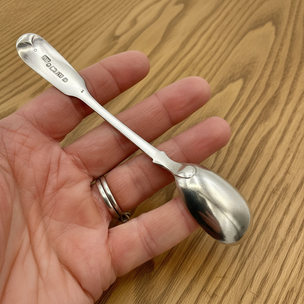 Back of antique silver salt spoon held in a hand with a wood background 
